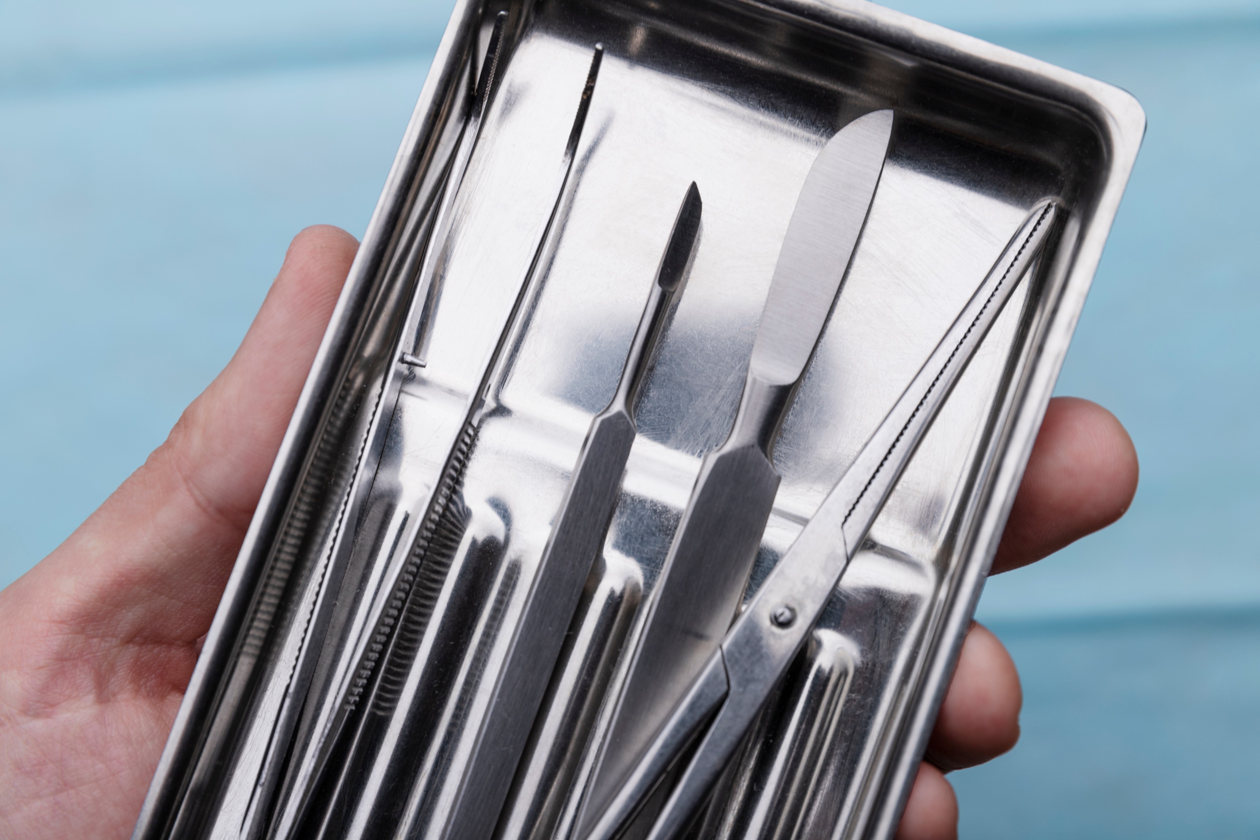 close-up-hand-holding-tray-with-medical-scalpel-tools